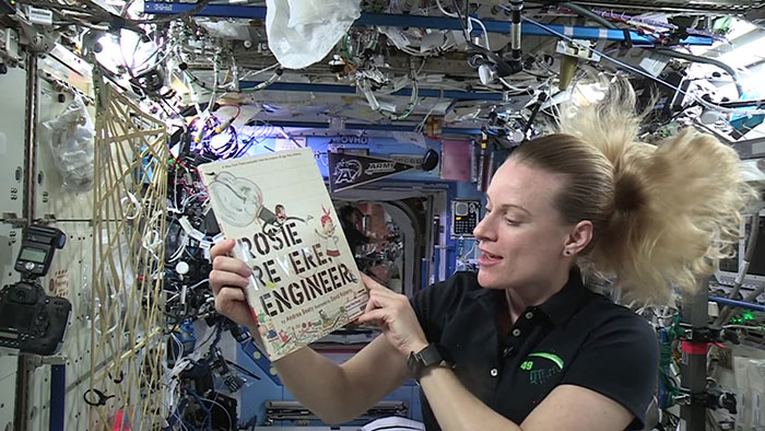 A female astronaut on the International Space Station reads the book Rosie Revere, Engineer by Andrea Beaty