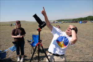 Man in front of solar telescope looks up and points at the Sun